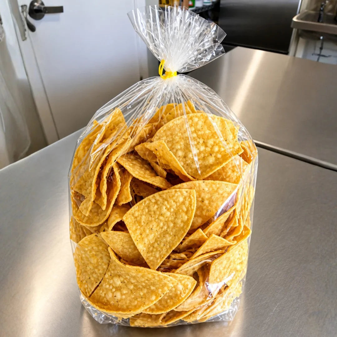 Large clear bag of fresh house-made tortilla chips tied with a yellow twist tie, sitting on a stainless steel prep table.