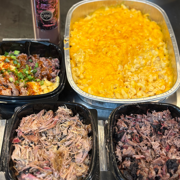Assorted food items including macaroni and cheese, pulled meat, and a bottle of sauce on a table.