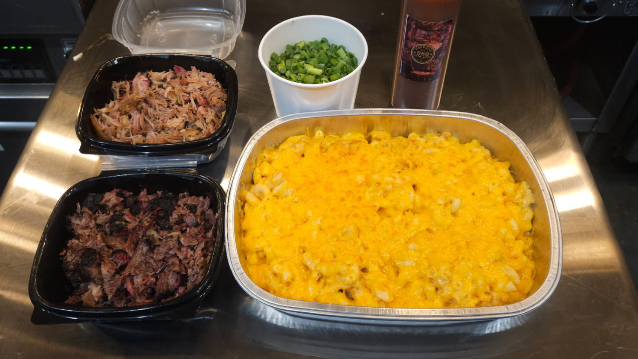 Prepared food items including macaroni and cheese, ground meat, and a container of greens on a metallic surface.